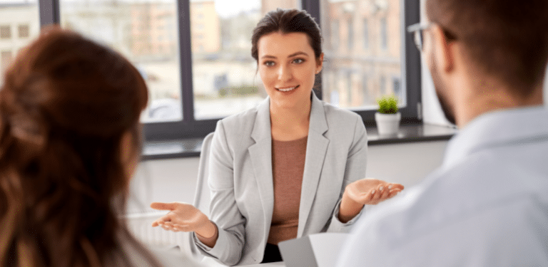 A woman in a light grey blazer actively engages in a conversation with two other individuals.