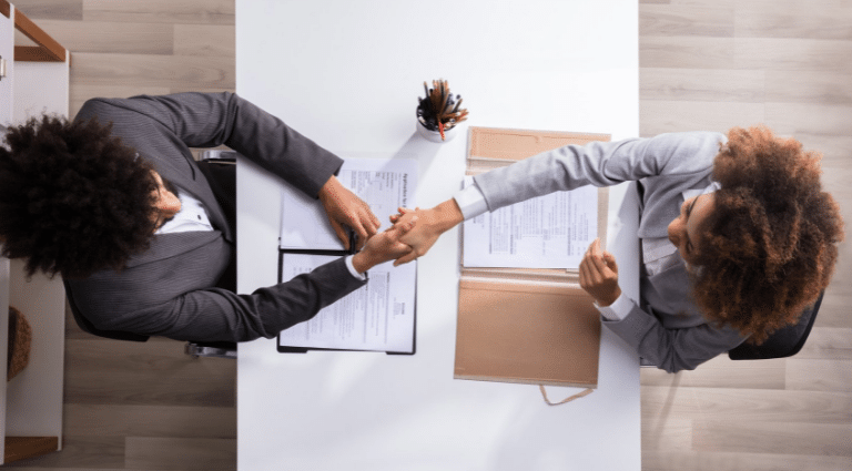 Overhead view of two businesspeople shaking hands across a table with documents.