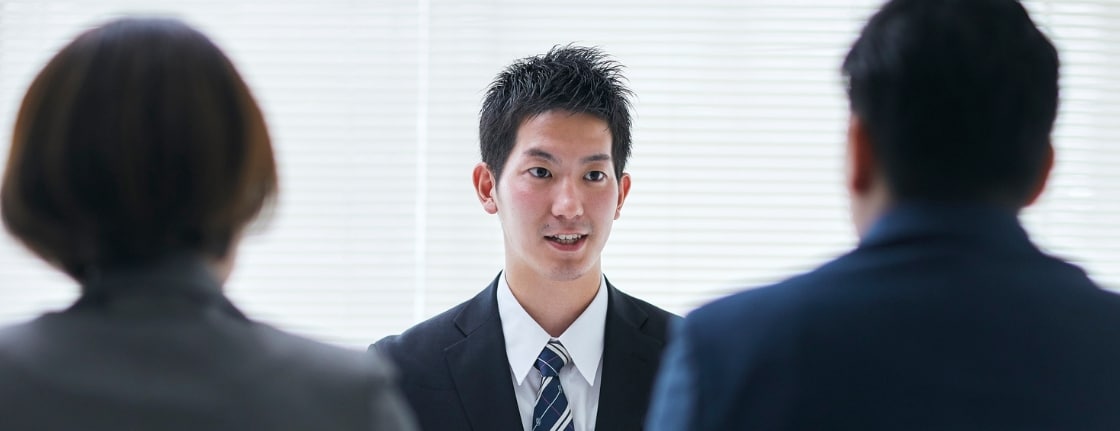 Young man in a suit explains something to two colleagues in a bright office meeting room